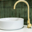 White sink with gold faucet against a green tiled wall