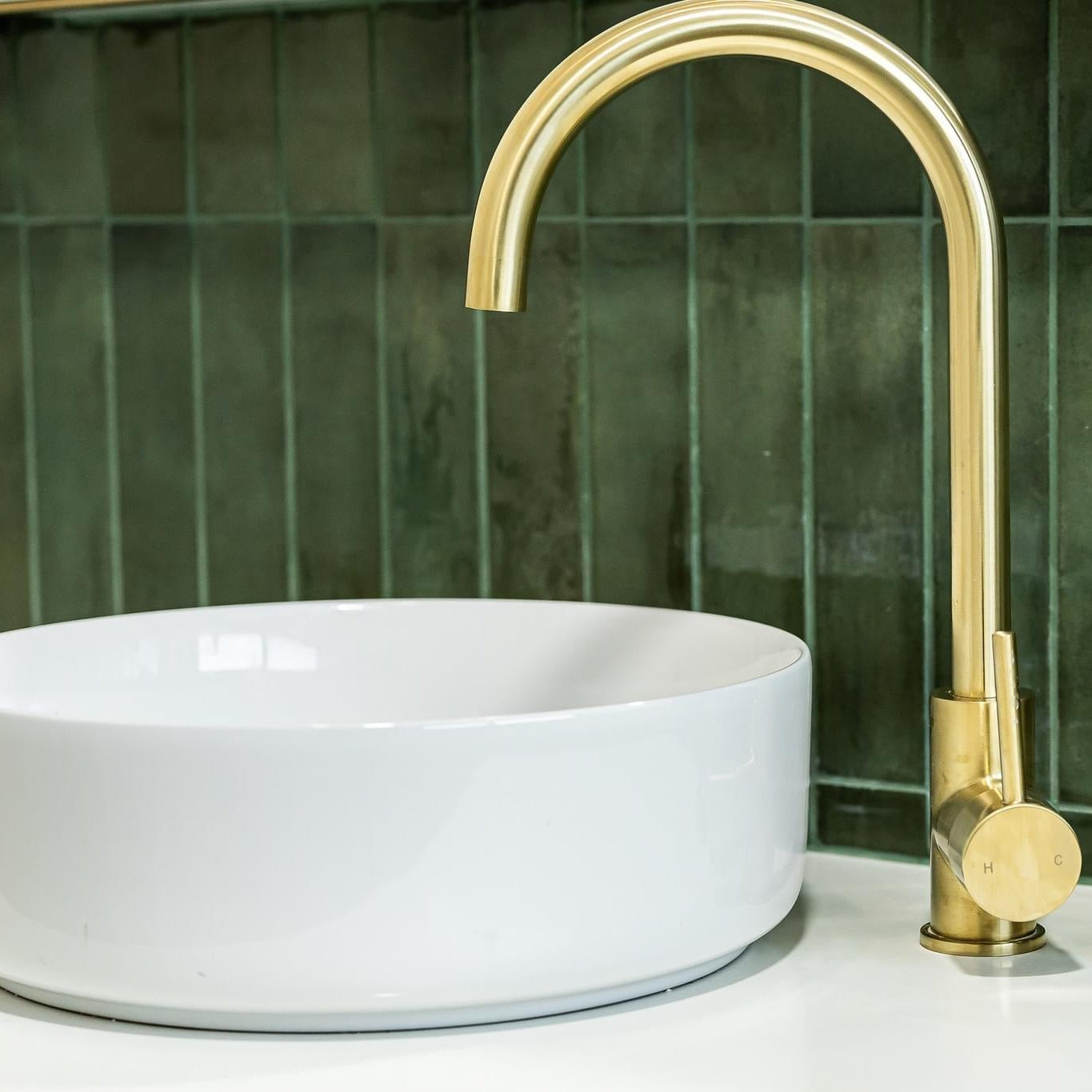 White sink with gold faucet against a green tiled wall