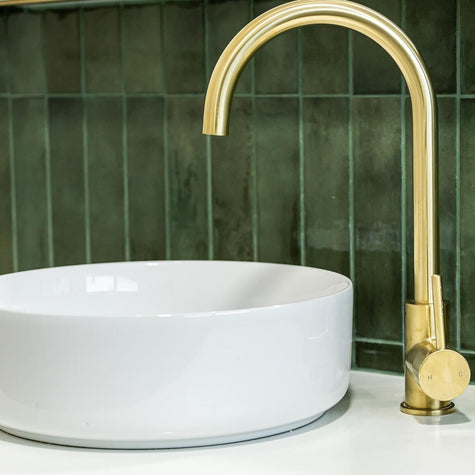 White sink with gold faucet against a green tiled wall