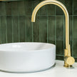 White sink with gold faucet against a green tiled wall