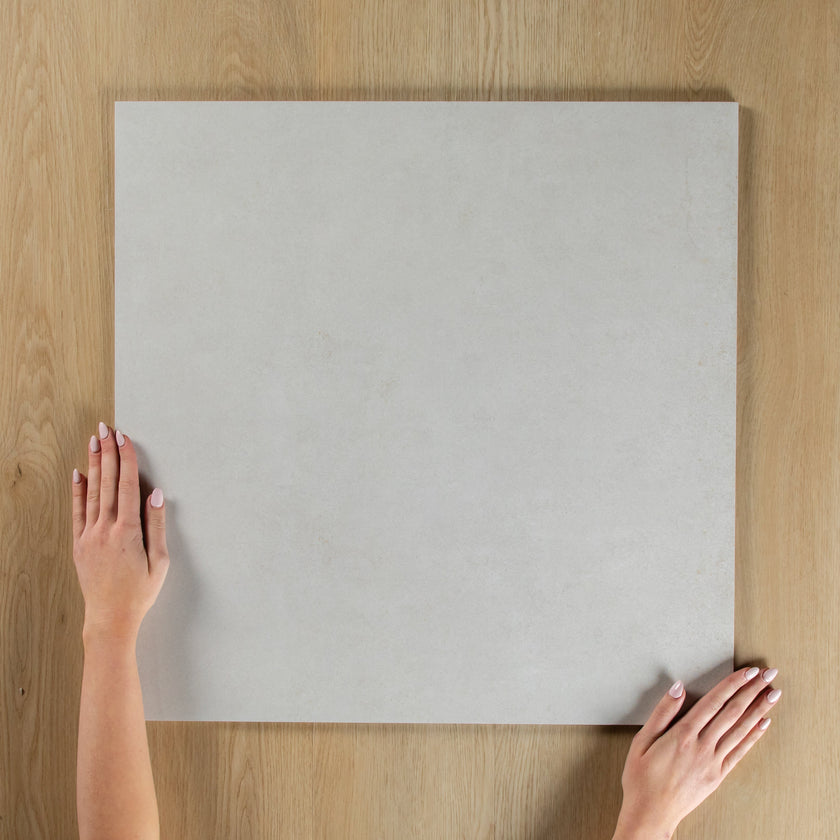 Person holding a light gray square tile on a wooden surface